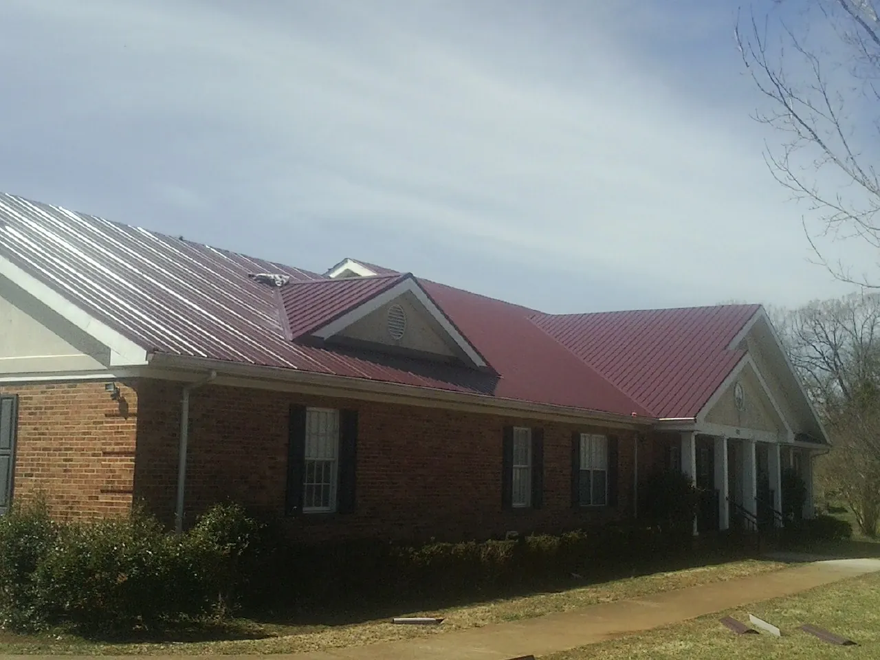 Red metal roof with gabled entries on a long brick building, from a Hail Damage Roof Repair job in Hurley