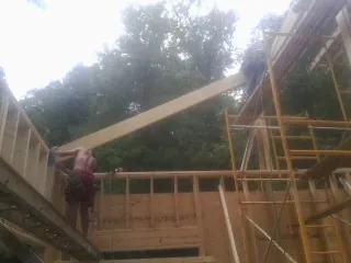 Carpenter raising a rafter beam on a new second story frame in Hurley