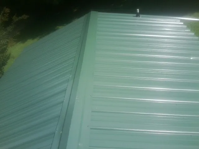 New green metal panels meeting at the ridge of a roof — Flat Roof Repair work by our crew in Hurley