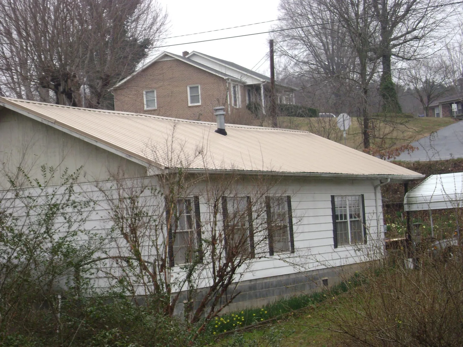 Tan metal roof on a white sided house set into a hillside — Commercial Roofing by Roofing Brothers in Hurley