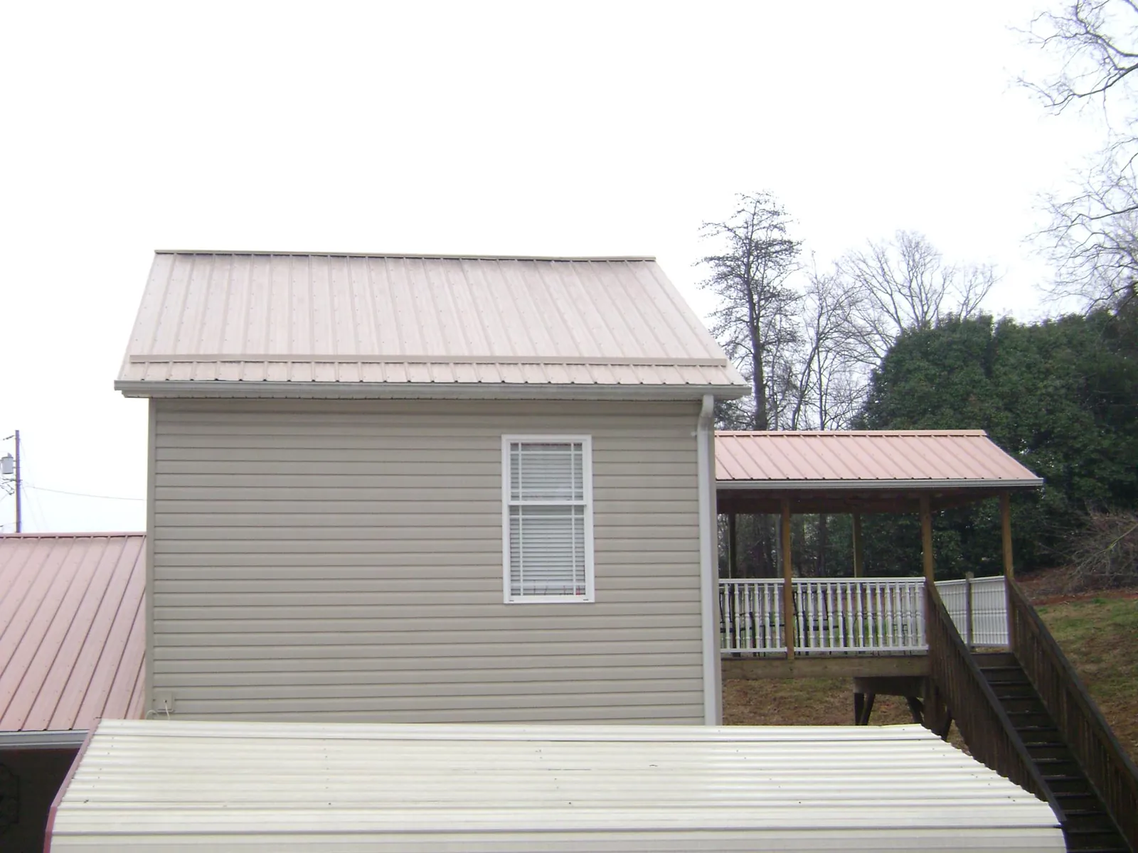 Tan metal roofs on a two story addition and attached porch, from a Roof Replacement job in Hurley